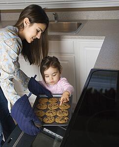 Caucasian mother and daughter taking cookies out of oven.