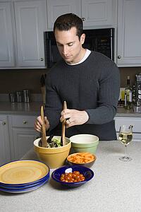Caucasian man making salad on kitchen counter.