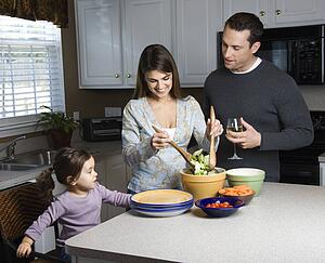 Woman making salad on kitchen counter with daughter and husband