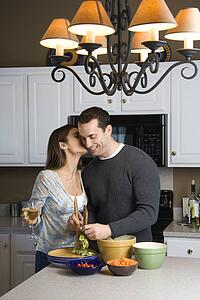 Caucasian woman kissing man at kitchen counter.