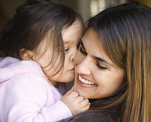 Caucasian mother holding daughter kissing her cheek and smiling.