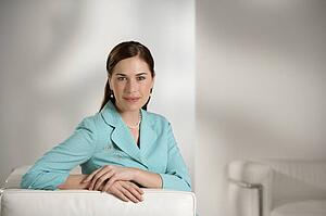 Caucasian mid adult professional business woman sitting in modern office looking at viewer and smiling.