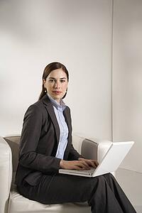 Mid adult professional business woman sitting in modern office working on laptop looking at viewer