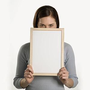 Caucasian mid adult professional business woman peeking over top of blank dry erase board in front of her face.