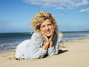 Woman lying in sand on beach with head resting on hands smiling