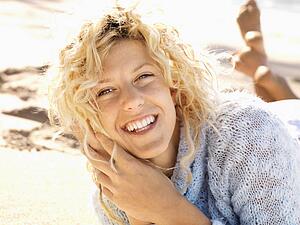Woman lying in sand on Maui, Hawaii beach smiling.