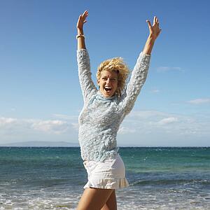 Portrait of attractive young blond woman smiling with arms raised in air on Maui, Hawaii beach.