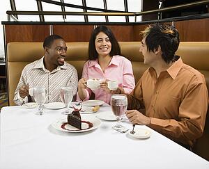 Small group of mid adult friends at restaurant talking and having dessert