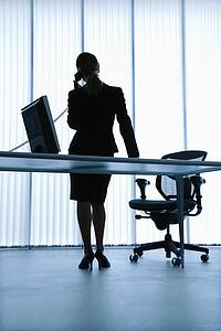 Silhouette of Caucasian businesswoman standing at computer desk on telephone.