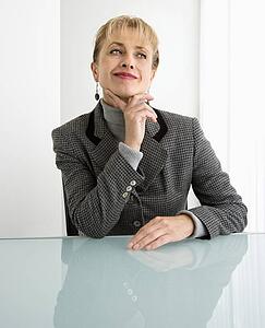 Woman sitting at desk with hand to chin smiling and making facial expression
