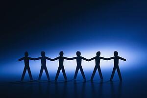 Silhouette of cutout paper men standing holding hands.