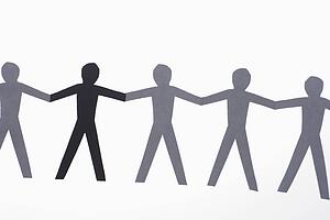 One black cutout paper person holding hands with group of white people