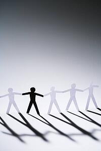 One black cutout paper person holding hands with group of white people