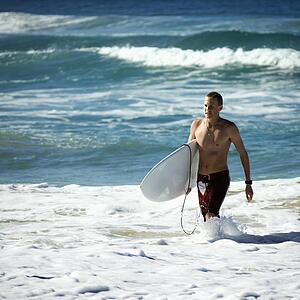 Male walking ocean carrying surfboard in Surfers Paradise, Australia
