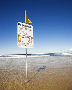 Sign and flag on beach in Surfers Paradise, Australia with lifeguard schedule.