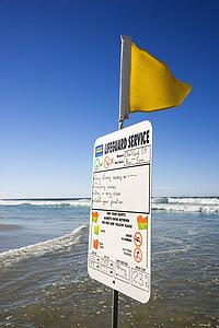 Sign and flag on beach in Surfers Paradise, Australia with lifeguard schedule