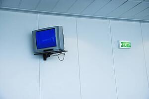 Monitor mounted to wall next to exit sign in airport