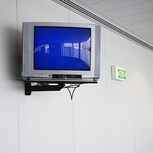 Monitor mounted to wall next to exit sign in airport