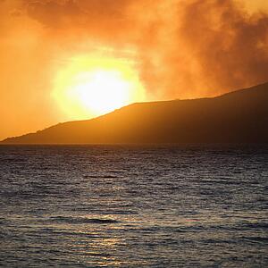 Sun setting behind mountain with ocean