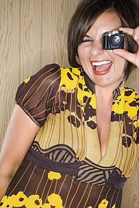 Woman looking through miniature toy camera and making facial expression