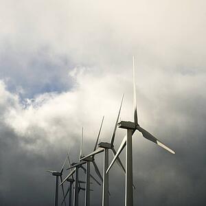 Row of turbines at wind farm against cloudy gray sky