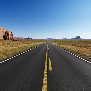 Open highway in scenic desert landscape with distant mountains and mesas