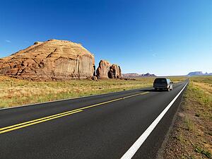 Sport utility vehicle on open highway in scenic desert landscape with butte land formation