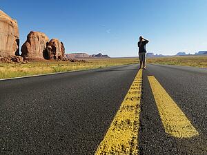 Teenage boy taking photograph standing in open road in the desert with landforms