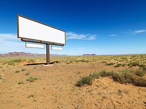 Blank billboard in middle of desert landscape with distant mountains.