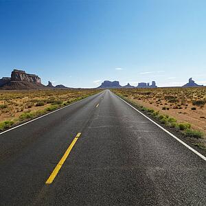 Open road in scenic desert landscape with distant mountains and mesas