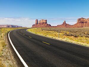 Curving scenic desert road with mesa land formations and mountains in the background