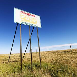 South Dakota road sign with Mount Rushmore graphic in rural field