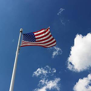 American flag flying with cumulus cloud formation in blue sky