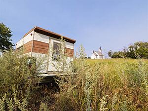 Recreational vehicle in overgrown field with rural church in distance