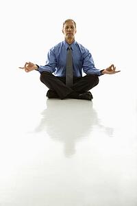 Caucasian middle aged businessman meditating in yoga lotus pose on floor.