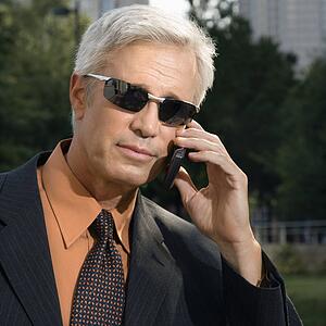 Caucasian middle aged businessman in sunglasses talking outdoors on cell phone.