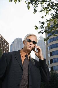 Middle aged businessman in sunglasses talking outdoors on cell phone
