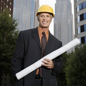 Middle aged businessman holding blueprints wearing hard hat 