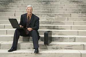 Businessman sitting on steps outdoors with laptop and briefcase