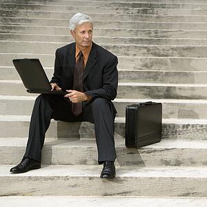 Businessman sitting on steps outdoors with laptop and briefcase