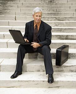 Businessman sitting on steps outdoors with laptop and briefcase