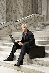 Businessman sitting on steps outdoors with laptop and briefcase