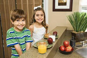 Brother and sister sitting at kitchen bar with healthy breakfast