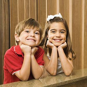 Hispanic children with their head on hands smiling at viewer. 