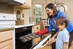 Side view of Hispanic mother and son putting cookies into oven.
