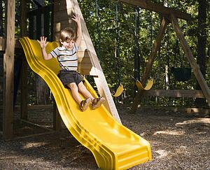 Boy sliding down outdoor slide with arms raised above head