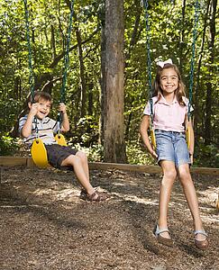 Hispanic boy and girl on swing set smiling at viewer.