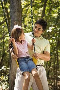 Father pushing daughter on swing and making eye contact