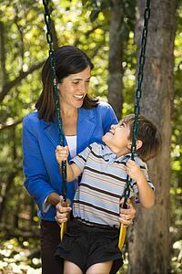 Mother pushing son on swing and making eye contact