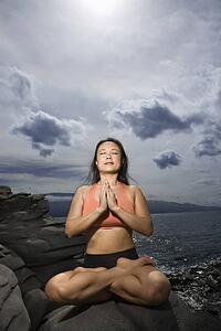 Woman sitting on rock by ocean in lotus pose with eyes closed in Maui, Hawaii